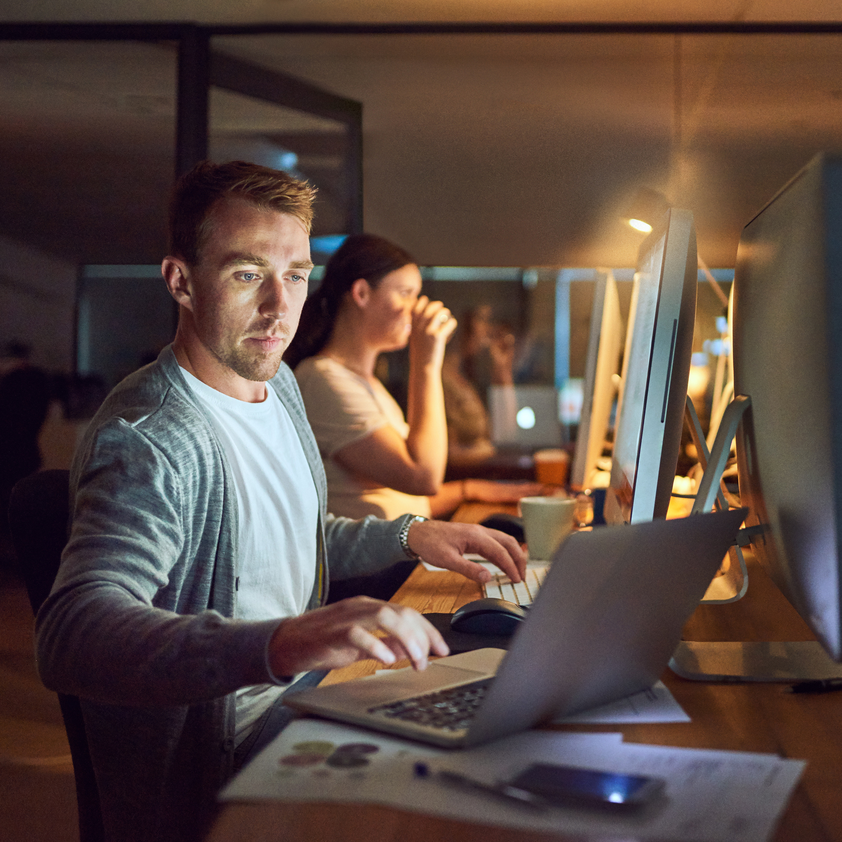 Shot of a young man using a computer and laptop during a late night in a modern office